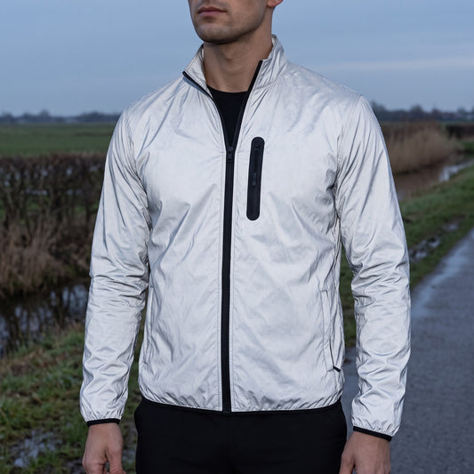 Reflective running jacket for men worn on a wet path at dusk, the whole silver shell catching the last light