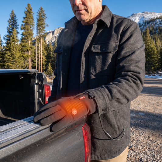 Heated gloves worn by a man resting his hand on a frosty pickup truck at a Colorado Rockies trailhead on a cold winter morning